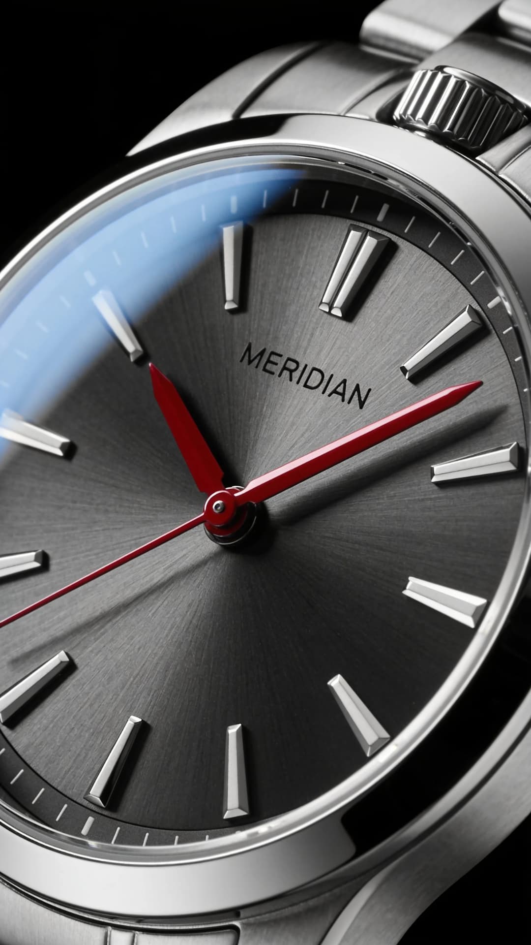 Close crop of a MERIDIAN wristwatch with a brushed silver dial, red hands and a steel bracelet against black