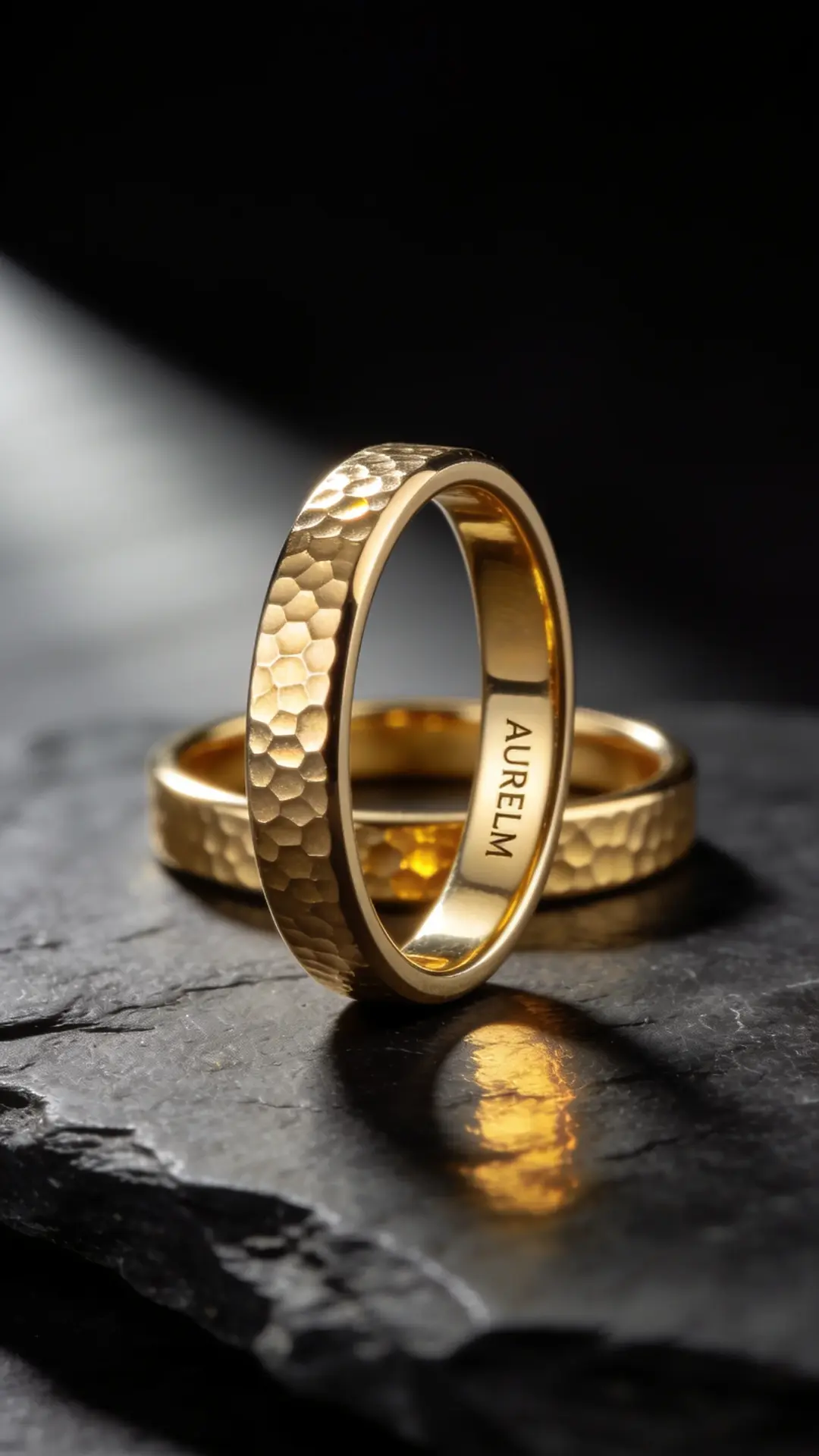 Hammered gold AURELM band standing on dark slate, a second ring lying flat behind it